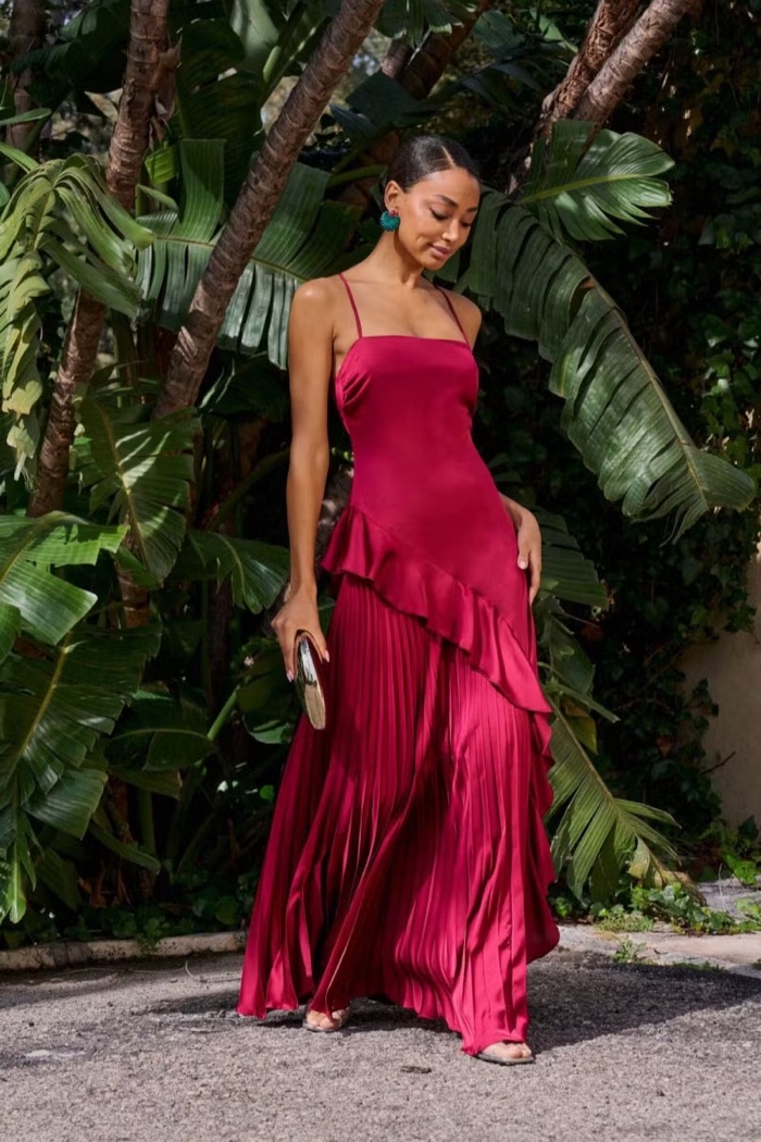 Woman in a deep raspberry satin dress with ruffled hem among palms