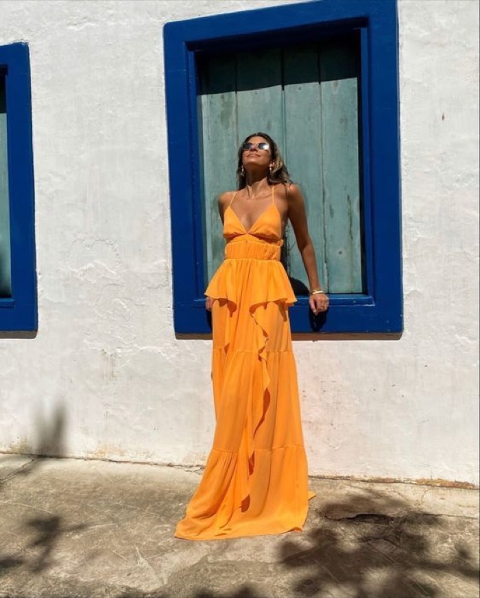 Woman in a flowing tangerine maxi dress against a blue window